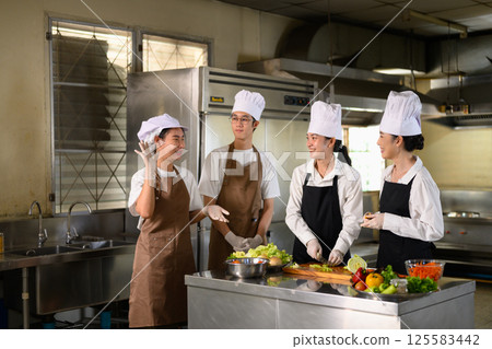 Young chefs collaborating on food preparation during hands on cooking class at culinary school 125583442