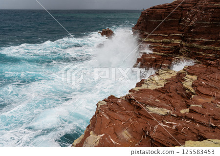 Red rock cliff in Cala Rossa, Terrasini, coastal landscape with waves crashing on red rock cliffs Red rock cliff in Cala Rossa, Terrasini, coastal landscape with waves crashing on red rock cliffs 125583453