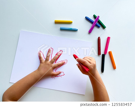 Child drawing hand outline with colorful crayons on white paper 125583457