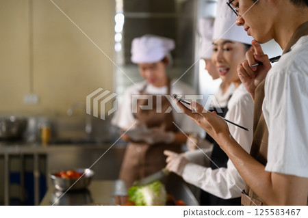 Culinary students collaborating and checking a recipe plan during a cooking class 125583467