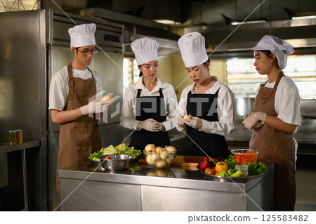 Young chefs collaborating on food preparation during hands on cooking class at culinary school 125583482