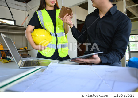Architects discussing material sample and reviewing design plans at a renovation site Architects discussing material sample and reviewing design plans at a renovation site 125583525