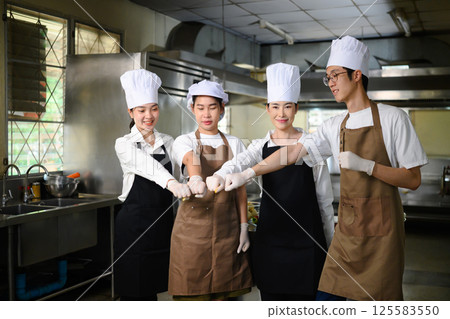 Group of students doing a team fist bump celebrating teamwork in culinary school kitchen Group of students doing a team fist bump celebrating teamwork in culinary school kitchen 125583550