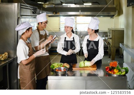 Cooking instructor guiding students in vegetable preparation during hands on class 125583556