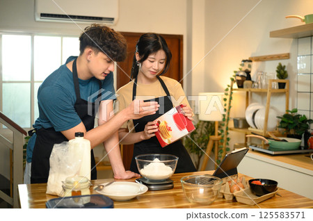 Happy young couple following recipe and measuring pancake mix together in a kitchen 125583571