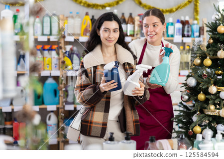 Young saleswoman offering spray cleaner to girl in store decorated for Xmas 125584594