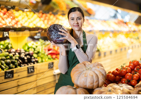 Middle-aged female seller offering red cabbage in grocery market 125584694