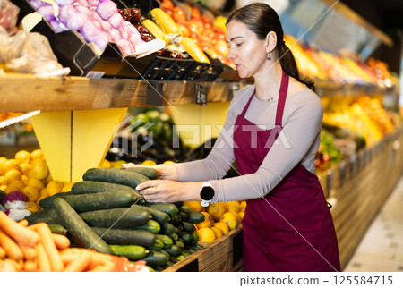 Middle-aged female seller putting cucumbers on counter in grocery market 125584715