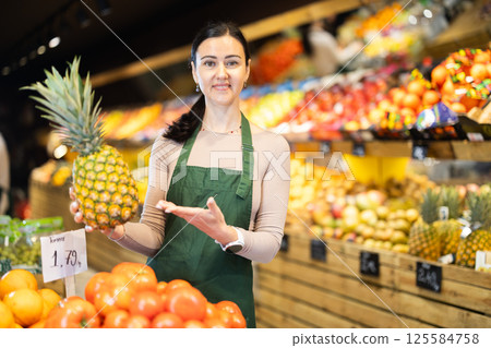 Middle-aged female seller offering pineapple in grocery market 125584758
