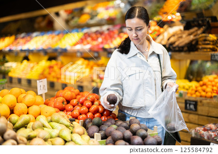 Middle-aged woman choosing avocado in grocery store Middle-aged woman choosing avocado in grocery store 125584792