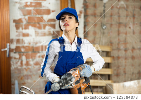 Workwoman standing at construction site with pneumatic chisel hammer 125584878