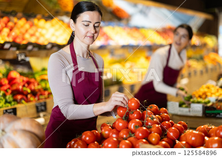 Woman staff with tomato working in greengrocery Woman staff with tomato working in greengrocery 125584896