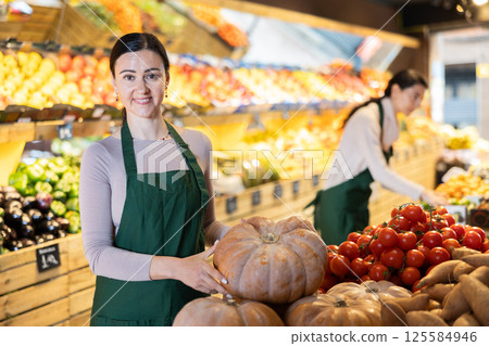 Adult woman seller offers pumpkin in vegetable shop Adult woman seller offers pumpkin in vegetable shop 125584946