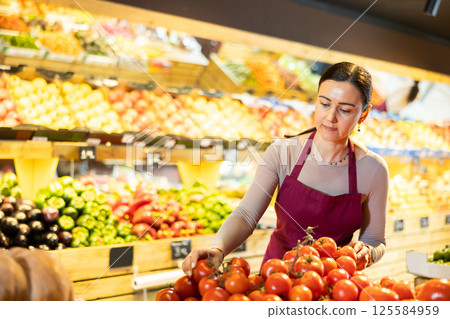 Supermarket employee carefully places ripe tomatoes on shelves of grocery supermarket 125584959
