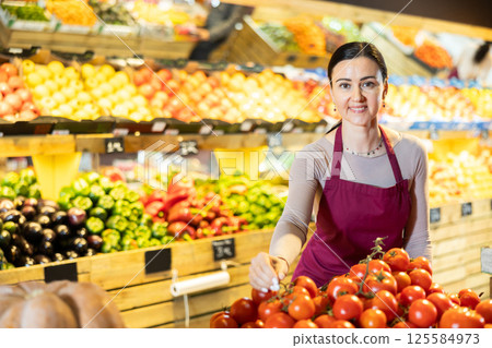 Middle-aged female seller putting tomatoes on counter in grocery market 125584973