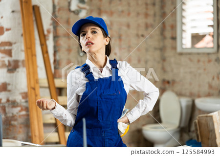 Portrait of confident female foreman in blue overalls in building under construction Portrait of confident female foreman in blue overalls in building under construction 125584993