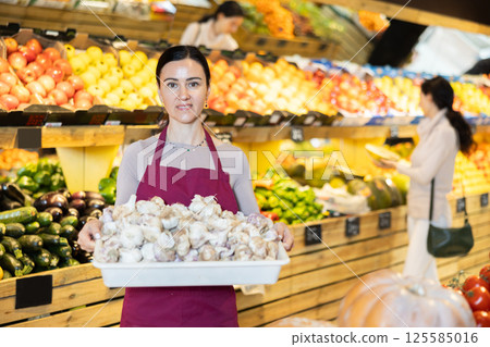 saleswoman holds a container of garlic in her hands 125585016