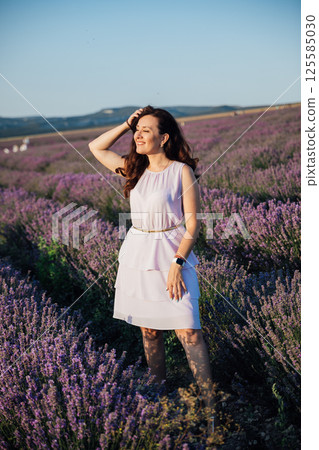 Woman in a dress walking in summer in a field of fragrant lavender Woman in a dress walking in summer in a field of fragrant lavender 125585030
