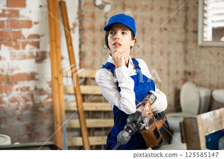Female builder confidently holding pneumatic jackhammer in house under construction Female builder confidently holding pneumatic jackhammer in house under construction 125585147