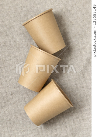 Disposable beige paper cups on a beige linen cloth top view, mockup. No plastic lifestyle Disposable beige paper cups on a beige linen cloth top view, mockup. No plastic lifestyle 125585149
