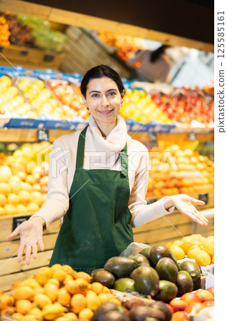 Female seller of fruit and vegetable store waits for visitors near counter Female seller of fruit and vegetable store waits for visitors near counter 125585161