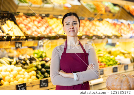 Middle-aged female seller standing by pumpkins in grocery market 125585172