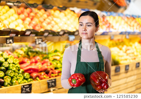 Middle-aged female seller offering red pepper in grocery market 125585230