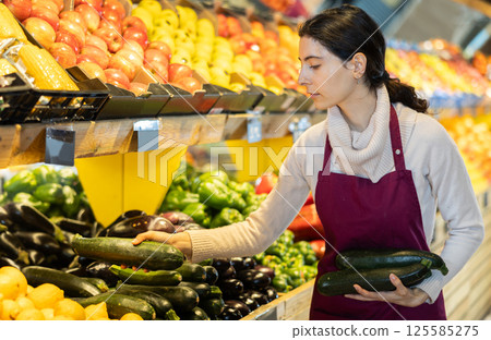 seller puts cucumbers on a shelf in a store seller puts cucumbers on a shelf in a store 125585275