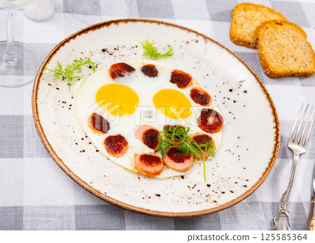 Spicy grilled sausages garnished with scrambled eggs fried close up 125585364