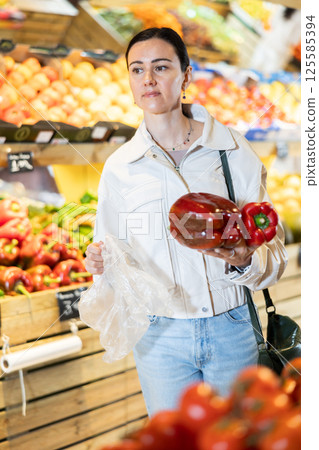 Middle-aged woman holding red peppers in grocery store Middle-aged woman holding red peppers in grocery store 125585394