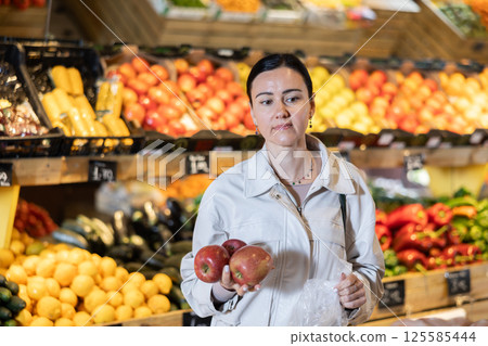 Portrait of female shopper carefully selecting ripe apples on supermarket display 125585444