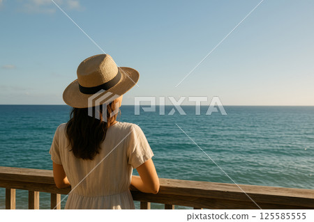 Caucasian woman in sun hat enjoying tranquil sea view from wooden balcony. concept of peaceful contemplation, ocean escape, relaxing moments, Copy space Caucasian woman in sun hat enjoying tranquil sea view from wooden balcony. concept of peaceful contemplation, ocean escape, relaxing moments, Copy space 125585555