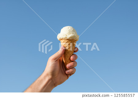 Hand holding ice cream cone against clear blue sky. concept of summer treats, simplicity, and joyful moments, Copy space 125585557