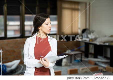 Female designer with papers working in apartment under renovation 125585570