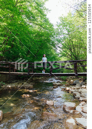 tourist standing on a mountain river bridge in a green forest tourist standing on a mountain river bridge in a green forest 125585654