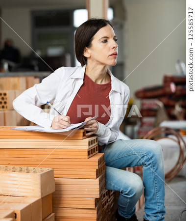 Female designer with papers working in apartment under renovation 125585717