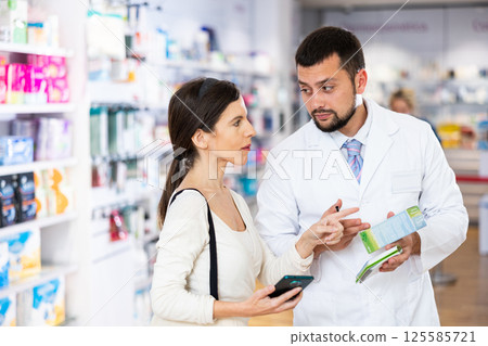 Druggist consulting woman client in pharmacy Druggist consulting woman client in pharmacy 125585721