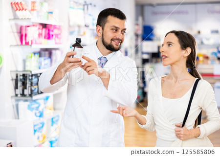 Pharmacist advises customer in pharmacy, offers medicine for body care Pharmacist advises customer in pharmacy, offers medicine for body care 125585806