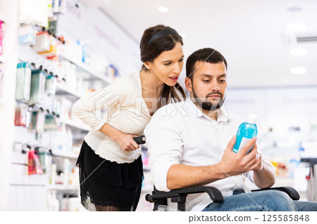 Man in wheelchair asks woman for help choosing the right medicine in pharmacy 125585848
