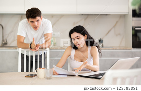 Sad girl works with laptop and paper documents and listens to reproaches of young guy Sad girl works with laptop and paper documents and listens to reproaches of young guy 125585851
