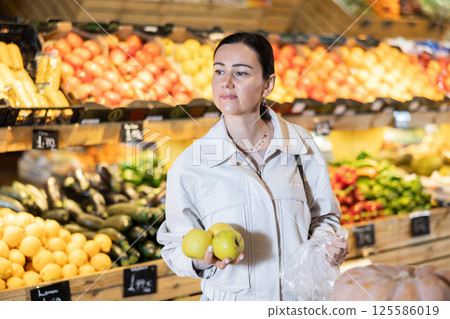 Portrait of female shopper carefully selecting ripe apples on supermarket display 125586019