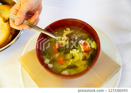 Womans hand takes hearty escudella barrejada soup out of plate with spoon 125586045