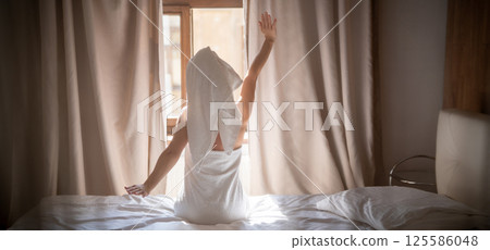 Back view of young woman in towel sitting on bed and meditating Back view of young woman in towel sitting on bed and meditating 125586048