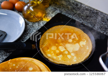 Frying pancakes in frying pan in kitchen Frying pancakes in frying pan in kitchen 125586067