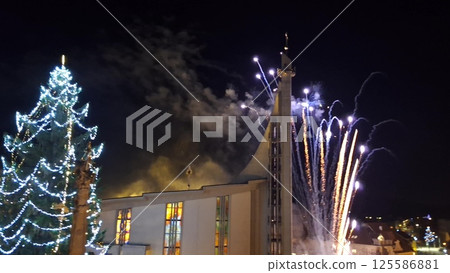 Fireworks during Christmas. View of the illuminated Christmas tree and fireworks over the church in the town Fireworks during Christmas. View of the illuminated Christmas tree and fireworks over the church in the town 125586881