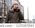 Portrait of mature woman in wool hat standing on the urban street, drinking takeaway coffee from paper cup. Middle-aged 40s female walking around the city at cold autumn day. Living in modern district 125587091