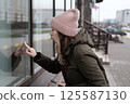 Portrait of mature woman in wool hat standing on the urban street, drinking takeaway coffee from paper cup. Middle-aged 40s female walking around the city at cold autumn day. Living in modern district 125587130