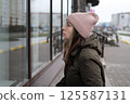 Portrait of mature woman in wool hat standing on the urban street, drinking takeaway coffee from paper cup. Middle-aged 40s female walking around the city at cold autumn day. Living in modern district 125587131
