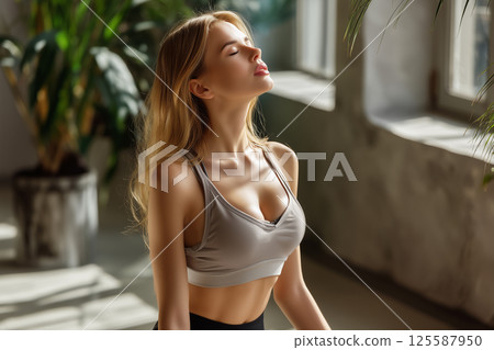 A young woman practices mindful breathing in a sunny room 125587950