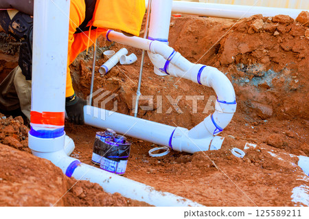 Contractor is engaged in laying down plastic sewage piping in trench at construction site during work day Contractor is engaged in laying down plastic sewage piping in trench at construction site during work day 125589211